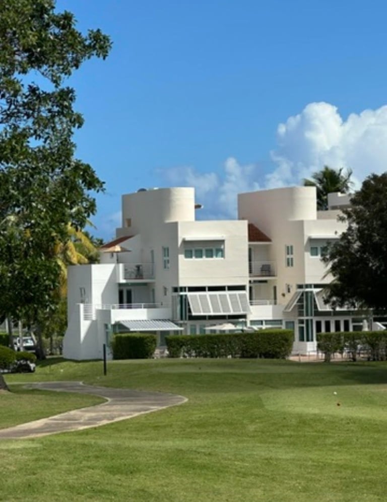 White modernist residential building with cylindrical towers, curved architecture, and manicured lawn surrounded by palm trees and greenery