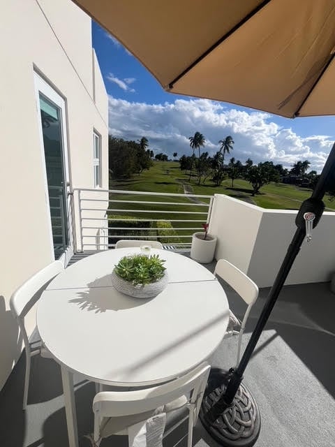 Modern balcony with white furniture and umbrella overlooking a golf course and tropical landscape