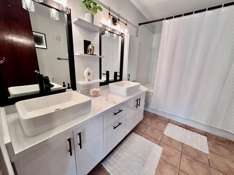 Modern bathroom with white vanity, dual vessel sinks, black-framed mirrors, and terracotta tile flooring