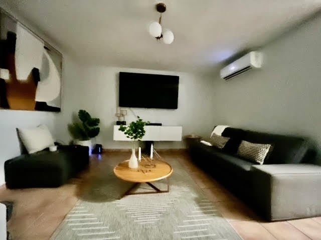 Modern living room with black sofas, round wooden table, wall-mounted TV, and minimalist decor
