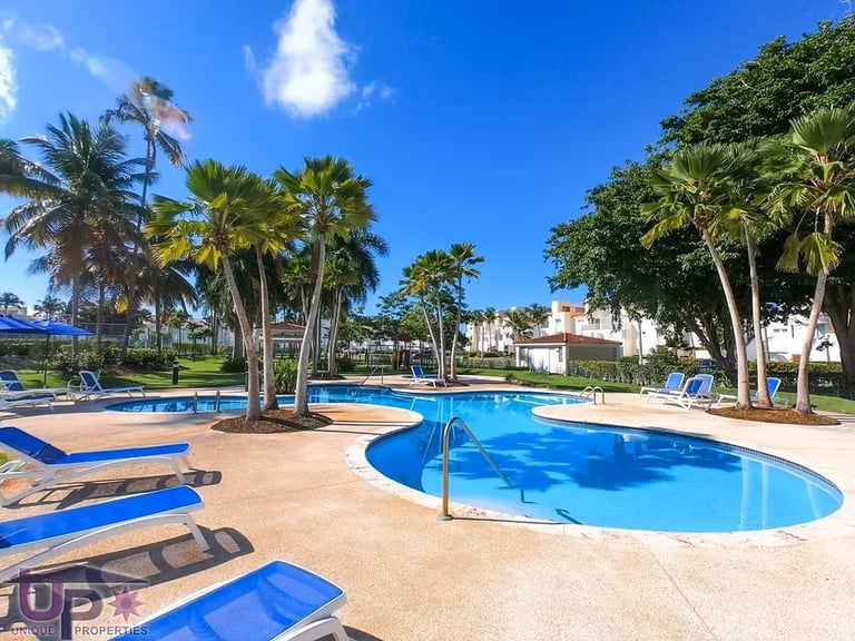 Resort pool with blue kidney-shaped swimming area, palm trees, loungers, and clear blue sky