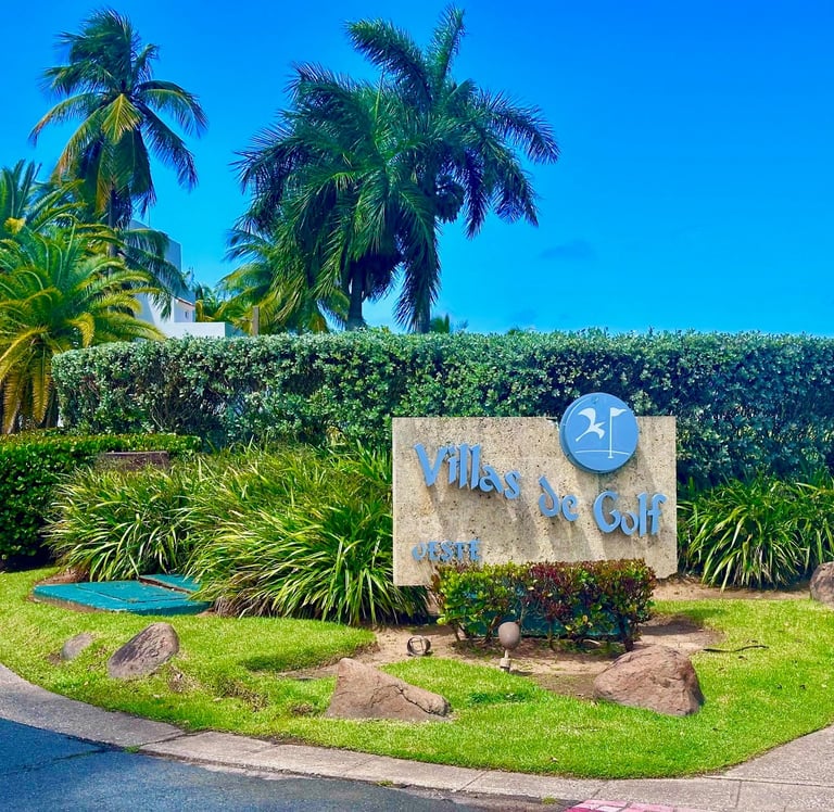 Waterfront golf course sign with palm trees and landscaping under blue sky