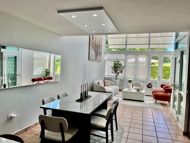 Modern living room and dining area with black table, comfortable seating, large windows, and contemporary lighting fixtures