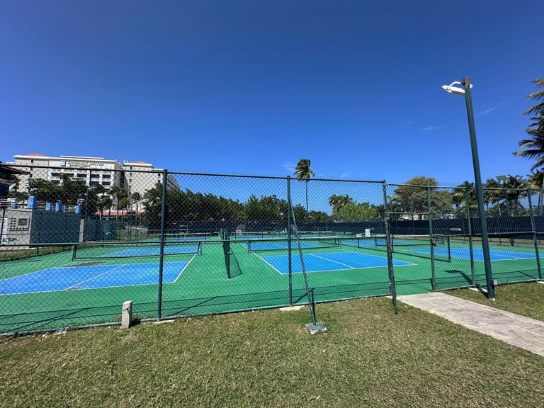 Outdoor tennis courts with blue and green surfaces enclosed by chain-link fencing on a sunny day
