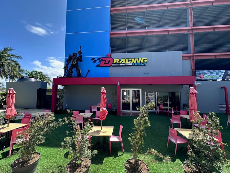 FD Racing storefront with pink and red exterior, outdoor seating area with green lawn, blue building facade visible behind