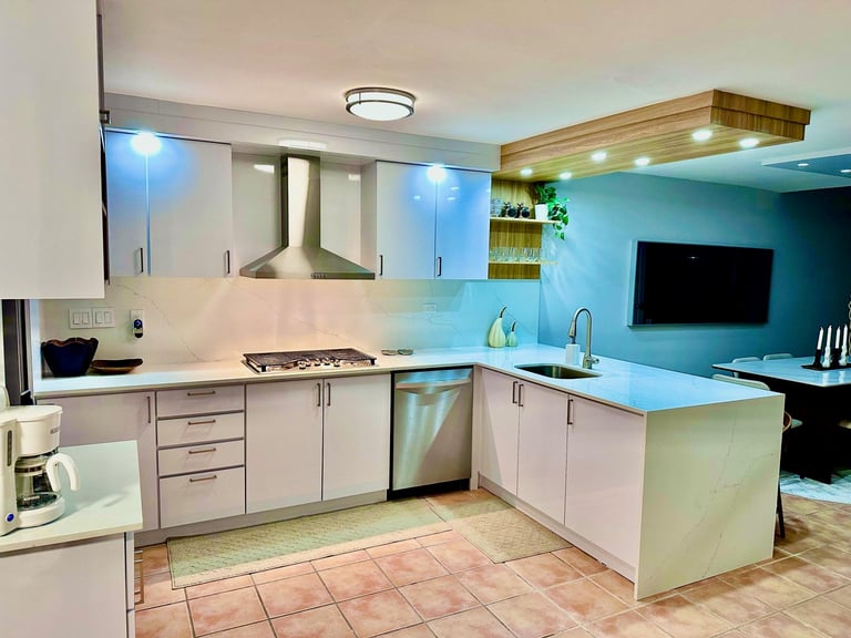 Modern kitchen with white cabinets, blue backsplash, island counter, stainless steel appliances, and open concept living area