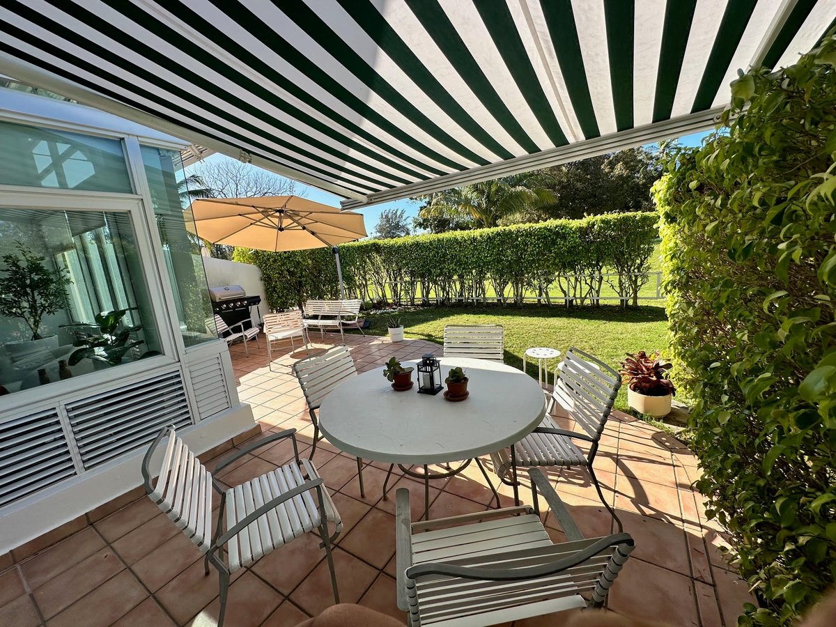Modern patio with striped retractable awning, round dining table, lounge chairs, and manicured hedge landscaping